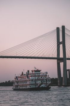 a large white boat floating on top of a river next to a tall suspension bridge