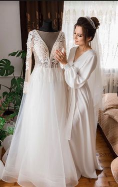 two women in wedding gowns standing next to each other and looking at the dress