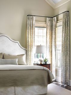 the bed is in front of two windows with drapes on them and curtains behind it