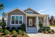 a gray house with white shutters and flowers on the front porch is surrounded by palm trees