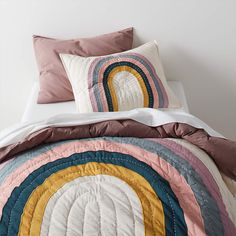 a bed with a quilt and pillows on top of it, in front of a white wall