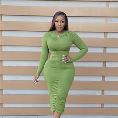 a woman standing in front of a wall with her hands on her hips wearing a green dress