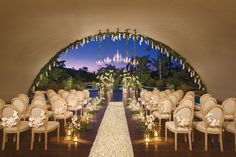 an outdoor ceremony setup with white flowers and chandeliers on either side of the aisle