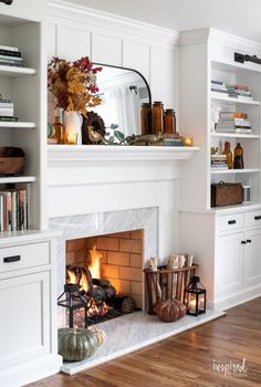 a fireplace with candles, bookshelves and pumpkins on the mantle next to it