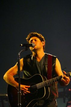 a man holding a guitar while standing in front of a microphone