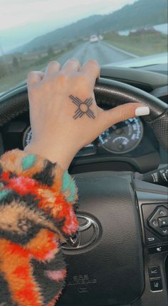 a person's hand on the steering wheel of a car with an arrow tattoo