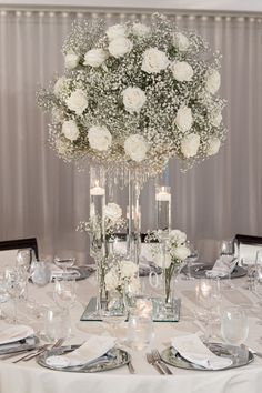 a centerpiece with white flowers and candles is on the table at a wedding reception