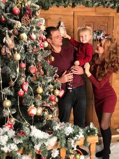 a man, woman and child standing in front of a christmas tree