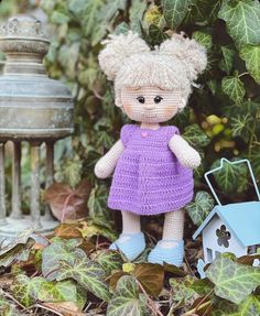 a crocheted doll is standing next to a birdhouse and potted plant