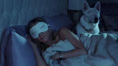 a woman laying in bed with a blindfold over her eyes and a dog sitting next to her