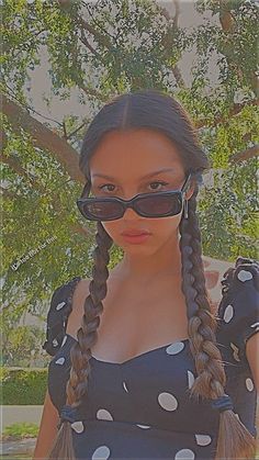 a woman with long hair wearing sunglasses and a polka dot dress is standing in front of a tree