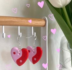 two red and pink heart shaped earrings hanging from hooks on a wall next to tulips