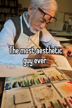 an older man sitting at a table with paint brushes and watercolors on it