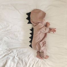 a baby in a dinosaur costume laying on a bed