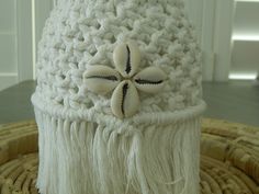 a white crocheted hat with tassels and flowers on the top is sitting on a wicker basket