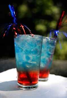 two glasses filled with red, white and blue drinks sitting on top of a table