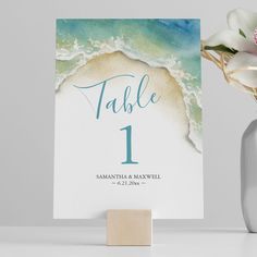 a table number card sitting next to a vase with flowers