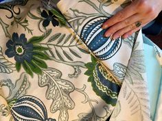 a woman is cutting fabric with scissors on a tablecloth that has blue and green flowers