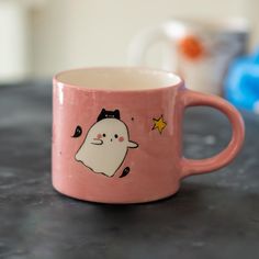 a pink coffee mug with a white ghost on the front and yellow stars on the back