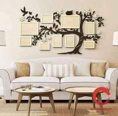 a white couch sitting under a tree with pictures on it's wall and two tables in front of it