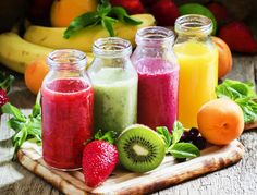 there are many different types of smoothies in glass jars on the table with strawberries and kiwis