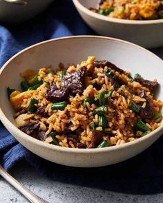 two bowls filled with rice and vegetables on top of a blue cloth next to silverware