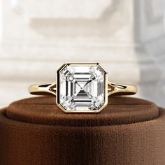 a diamond ring sitting on top of a brown velvet covered box next to a white wall