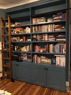 a book shelf filled with lots of books on top of a hard wood floor next to a ladder