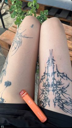 a woman's legs with tattoos and an orange pen on her left leg, sitting next to a bench