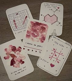 four handprinted cards with hearts and flowers are on a wooden table next to a calculator