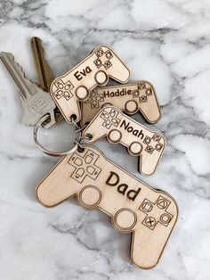 three wooden keychains with personalized video game controllers engraved on them, sitting on a marble surface