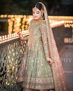 a woman in a green lehenga standing on a balcony with lights behind her