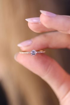 a woman's hand holding a diamond ring in front of her face and the other hand