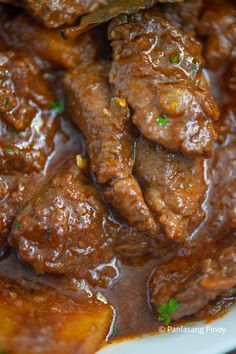 closeup of meat in gravy on a white plate with green garnish