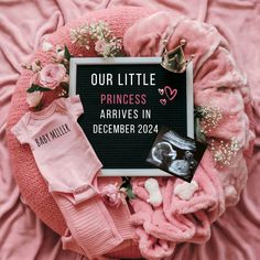 a baby announcement surrounded by pink blankets and other items, including a photo frame with the words our little princess arrived in december