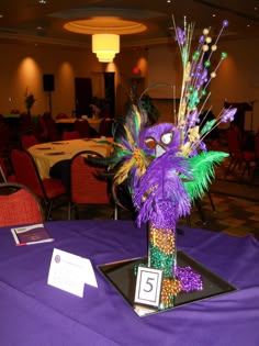 a purple table cloth topped with a vase filled with flowers and feathers on top of it