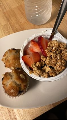 a bowl of granola, yogurt and strawberries on a plate with a spoon