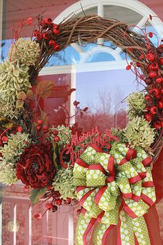 a wreath with red flowers and greenery on the front door is adorned with a green bow