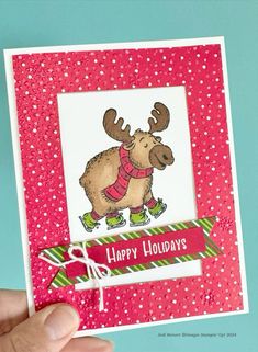 a hand holding up a christmas card with a moose on it