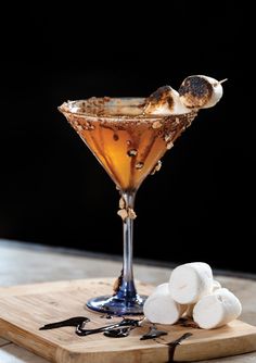 a drink with marshmallows on a cutting board next to some sort of appetizer