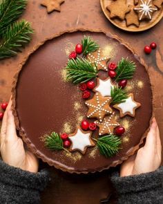 a person holding a chocolate cake decorated with christmas cookies and holly wreaths on it