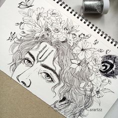 a drawing of a woman's face with flowers in her hair on top of a spiral notebook