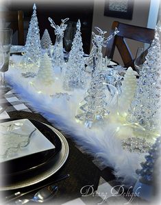 the table is set for christmas dinner with clear glass trees and white candlesticks