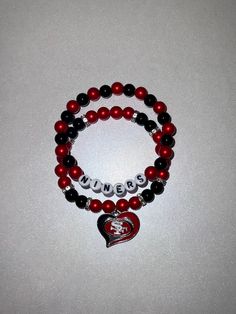 Show off your 49ers pride with this stunning handcrafted bracelet, designed in the team's iconic red and black colors. Made with smooth, high-quality beads, this double-strand bracelet features silver accents and "NINERS" spelled out in bold letters. The centerpiece is a heart-shaped charm with the 49ers logo, perfect for any die-hard fan. Whether you're attending a game or simply adding a touch of your favorite team to your outfit, this bracelet is a stylish and fun accessory for every 49ers supporter! Perfect for gifting or as a personal treat for yourself. 49ers Logo, Fan Jewelry, Foot Ball, Bead Ideas, Clay Bead, Presents For Men, Handcrafted Bracelets, Bracelets Handmade Beaded, Strand Bracelet