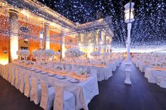 a banquet hall with tables and chairs covered in white linens, lit up by fairy lights