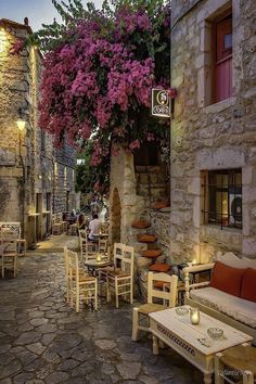 an alley way with tables and chairs on both sides, flowers growing over the wall