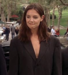 a woman in a black suit standing next to other people and cars on the street