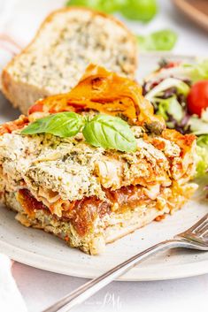 a white plate topped with lasagna sandwiches next to a bowl of salad and a fork