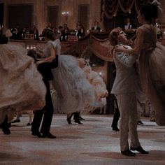 a man and woman dancing in a ballroom with other people standing around the dance floor