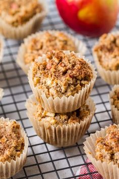 several muffins on a cooling rack with an apple in the background